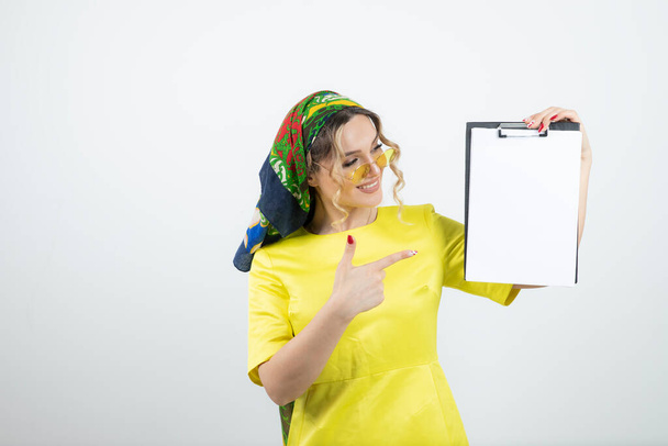 Photo of cute woman in headkerchief pointing at clipboard . High quality photo - Photo, Image