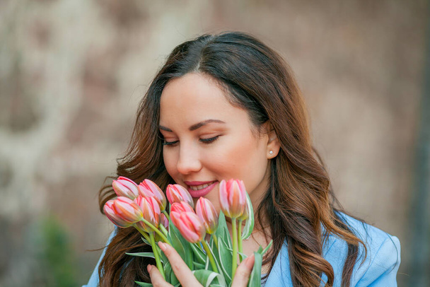 Porträt einer schönen jungen Frau im blauen Anzug mit einem Strauß Tulpen. - Foto, Bild