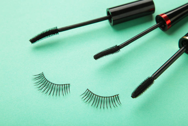 Close up of black eyeliners and mascara brush on mint background. Top view. - Photo, Image