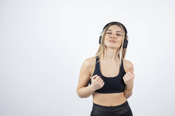 Athletic woman in crop top in headphones standing over wall. High quality photo - Fotó, kép