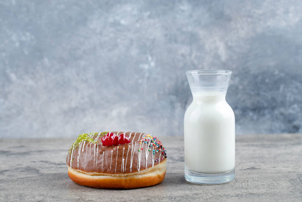 Donut de chocolate decorado con chispas y un vaso de leche fresca en la superficie de piedra. Foto de alta calidad - Foto, imagen