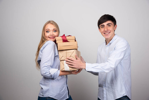 A férfi karácsonyi ajándékokat ad a barátnőjének a szürke falnál. Kiváló minőségű fénykép - Fotó, kép
