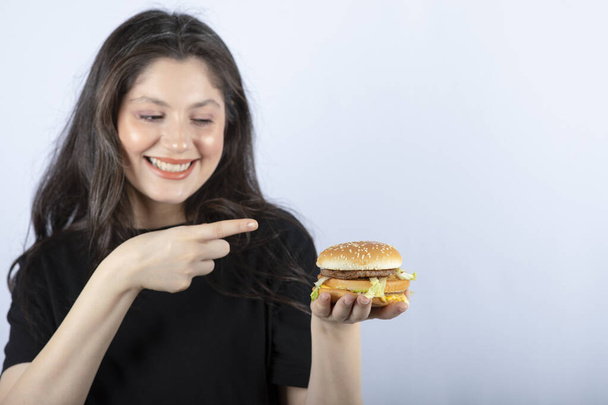 Photo of beautiful young woman pointing delicious meat burger. High quality photo - Photo, Image
