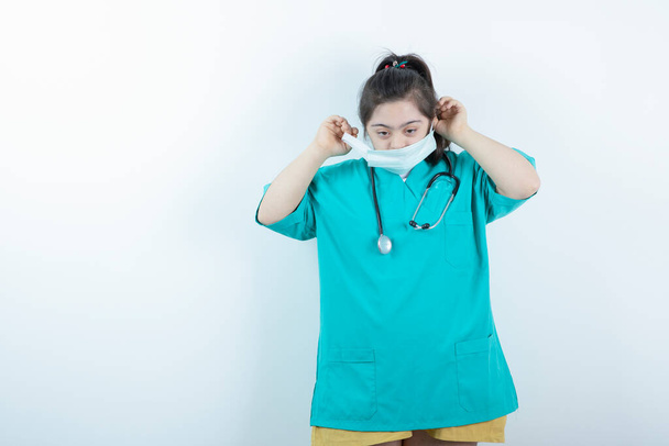 Jeune infirmière avec stéthoscope portant un masque médical contre un mur blanc. Photo de haute qualité - Photo, image