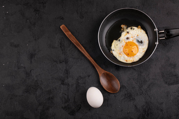 Heerlijke gebakken eieren in koekenpan met rauwe witte eieren op zwarte ondergrond. Hoge kwaliteit foto - Foto, afbeelding