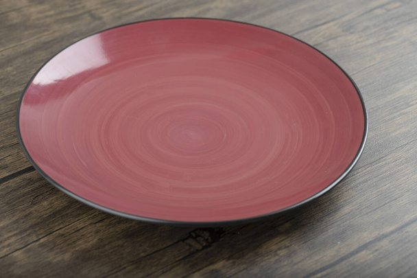 Červený prázdný keramický talíř umístěný na dřevěném stole. Kvalitní fotografie - Fotografie, Obrázek