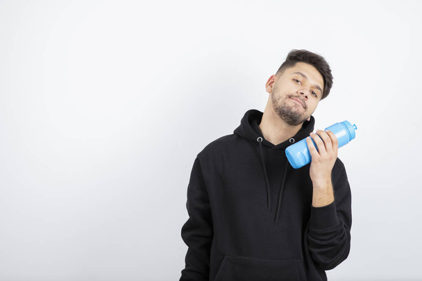 Retrato del joven guapo sosteniendo una mancuerna azul y una botella de agua. Foto de alta calidad - Foto, Imagen