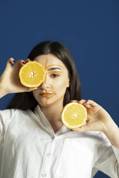 Image of young woman with painted face holding halved orange . High quality photo - Foto, imagen