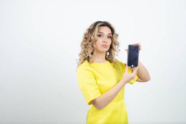 Photo of young woman with wavy hair in yellow dress holding her smartphone . High quality photo - Fotoğraf, Görsel