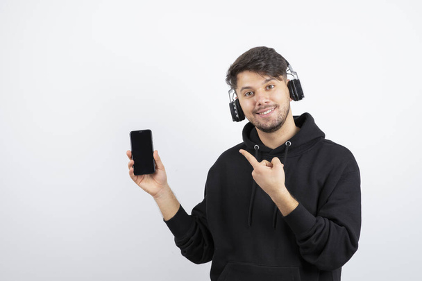 Schöner junger Mann mit drahtlosen Kopfhörern, der auf sein Handy zeigt. Hochwertiges Foto - Foto, Bild