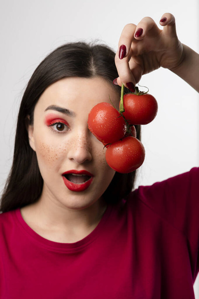 Kaunis tyttö pitelee punaisia tomaatteja silmän edessä. Laadukas kuva - Valokuva, kuva