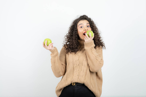 Afbeelding van krullende vrouw met rode lippenstift die groene appel eet. Hoge kwaliteit foto - Foto, afbeelding