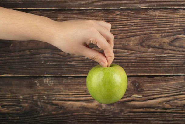 Male hand holding fresh green apple on wooden background. High quality photo - Fotografie, Obrázek