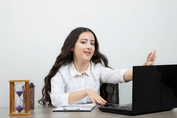 Jonge kantoormedewerker in witte blouse zittend aan bureau met laptop en poserend. Hoge kwaliteit foto - Foto, afbeelding