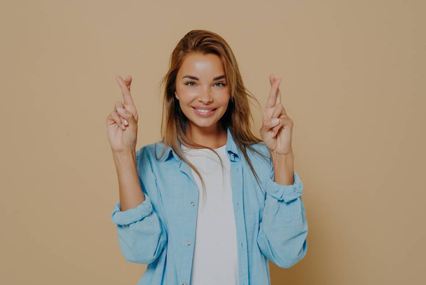 Positive lady with fingers crossed on beige background - Photo, Image
