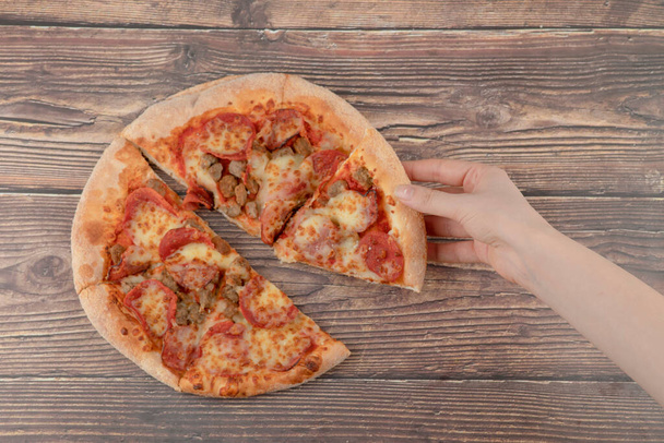 Female hand taking slice of pepperoni pizza on wooden table. High quality photo - 写真・画像