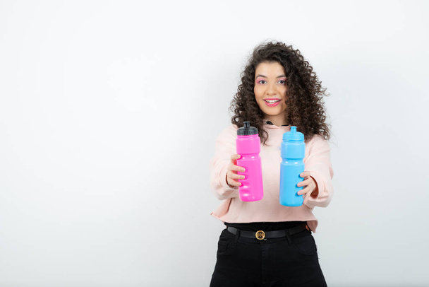 Young curly woman in sweater holding pink and blue water bottles. High quality photo - Photo, Image