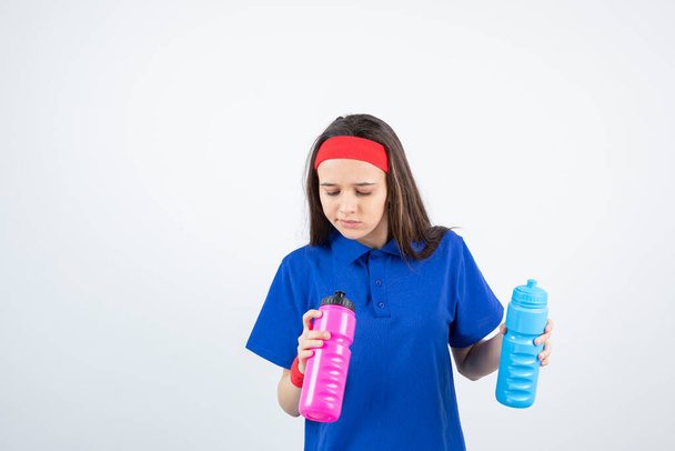 Φωτογραφία ενός νεαρού αθλητικού κοριτσιού που κρατάει πολύχρωμα μπουκάλια νερό. Υψηλής ποιότητας φωτογραφία - Φωτογραφία, εικόνα