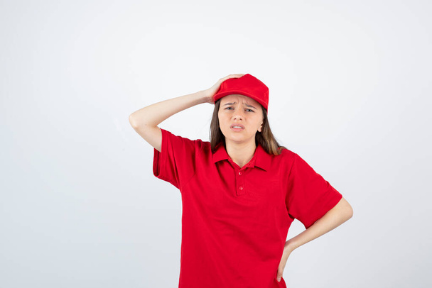 Φωτογραφία της νεαρής κούριερ με την κόκκινη στολή να κουράζεται μετά από πολλή δουλειά. Υψηλής ποιότητας φωτογραφία - Φωτογραφία, εικόνα