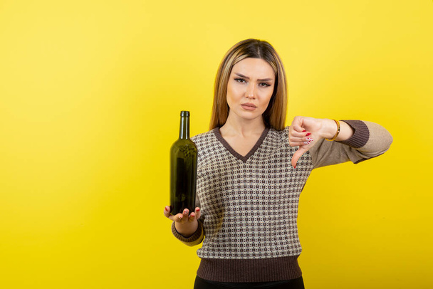 Egy fiatal nő képe egy üveg borral, aki hüvelykujját lefelé nyújtja. Kiváló minőségű fénykép - Fotó, kép