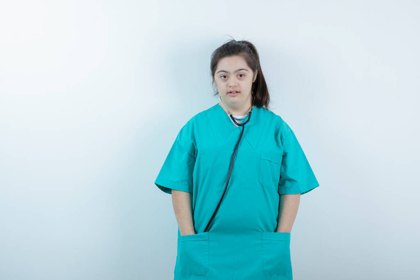 Jovem enfermeira de pé com estetoscópio contra a parede branca. Foto de alta qualidade - Foto, Imagem