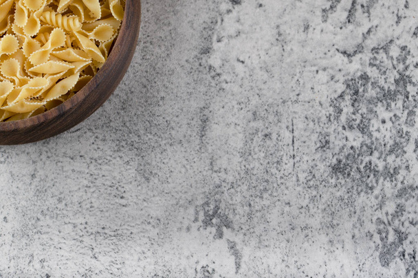 Wooden bowl of raw pasta placed on stone background. High quality photo - Zdjęcie, obraz
