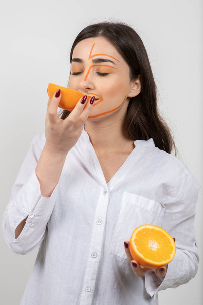 Imagen de mujer joven con la cara pintada sosteniendo la mitad de naranja. Foto de alta calidad - Foto, Imagen