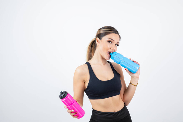 Mooie sportieve vrouw die flessen met water op een witte achtergrond vasthoudt. Hoge kwaliteit foto - Foto, afbeelding