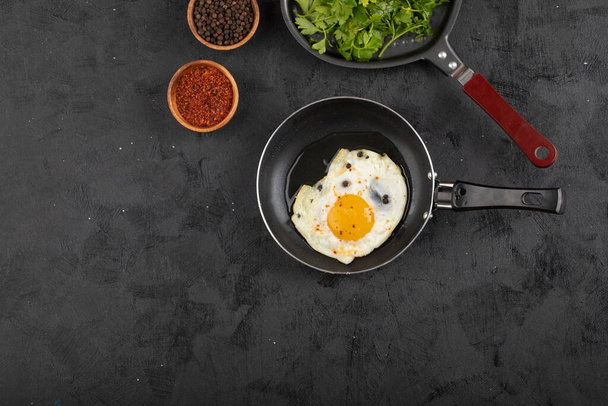 Gebratenes Ei auf Pfanne mit Gemüse und Gewürzen auf schwarzer Oberfläche. Hochwertiges Foto - Foto, Bild