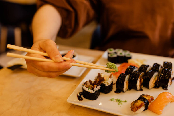 Las manos femeninas usan hábilmente los palillos en la mesa en el restaurante. Una persona irreconocible usa wasabi para sushi - Foto, imagen