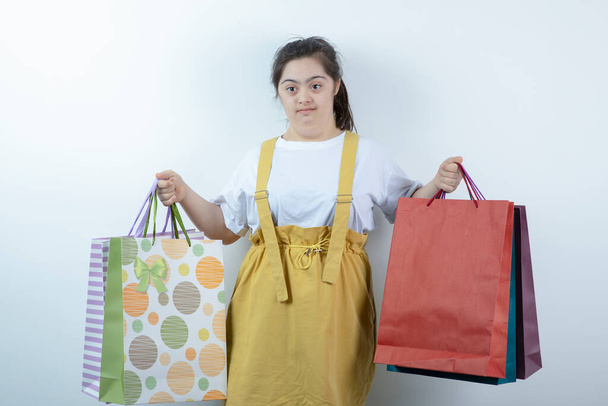 Adorable young girl with down syndrome holding shopping bags on white background. High quality photo - Foto, Imagem