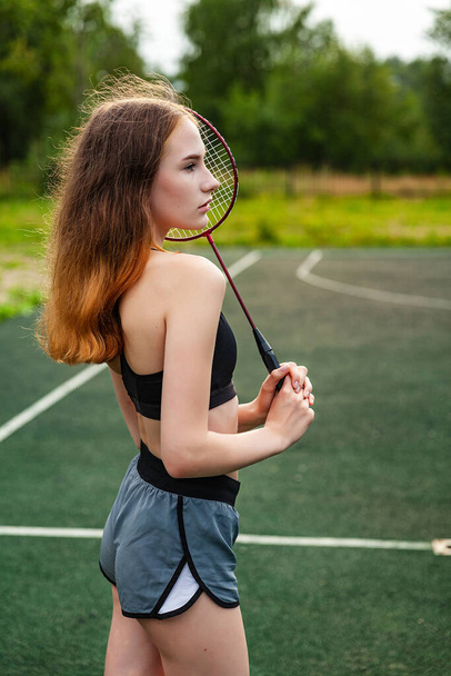 Young beautiful girl in sports top and shorts on the sports ground, posing on a sports ground. Daytime, fitness, open air, badminton, racket - Foto, imagen