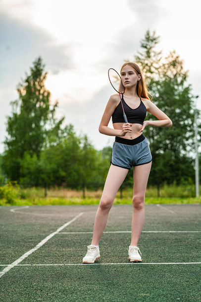 Young beautiful girl in sports top and shorts on the sports ground. Daytime, fitness, open air, badminton, racket - Photo, image