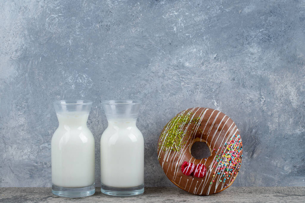 Chocolate glazed donut decorated with sprinkles and glass of fresh milk on stone surface. High quality photo - Photo, Image