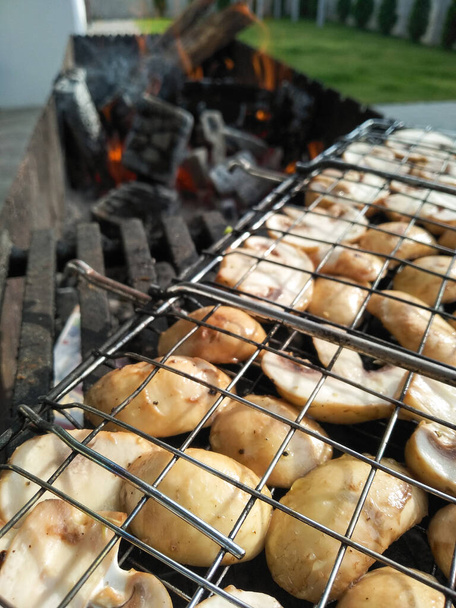 Gegrilde paddenstoelen roosteren op BBQ grill buiten. Gegrilde gerechten gebakken in houtskool grills. Lekkere heerlijke champignons worden op kolen gekookt. Zomer picknick concept. Vegetarisch menu. - Foto, afbeelding