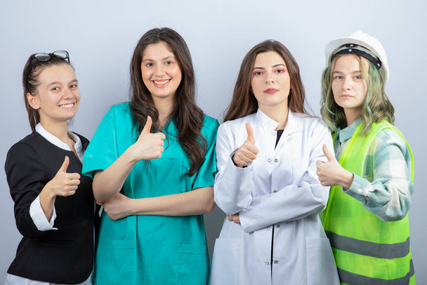 Młode kobiety z różnych zawodów stojące razem i podnoszące kciuki. Wysokiej jakości zdjęcie - Zdjęcie, obraz