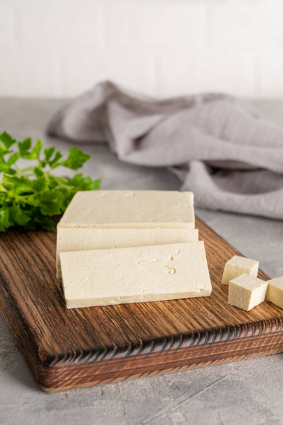 Свіжий сирний тофу з сої з петрушкою на дошці на сірому бетонному фоні. Веганський продукт. Копіювати простір
 - Фото, зображення