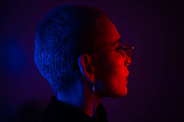 Portrait of beautiful young woman with short hair wearing glasses in neon light - Photo, Image