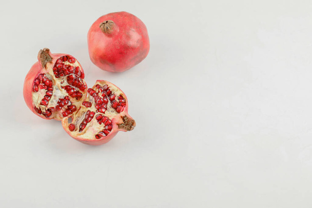 Geschnittene frische Granatäpfel mit ganzen Granatäpfeln auf weißem Tisch. Hochwertiges Foto - Foto, Bild