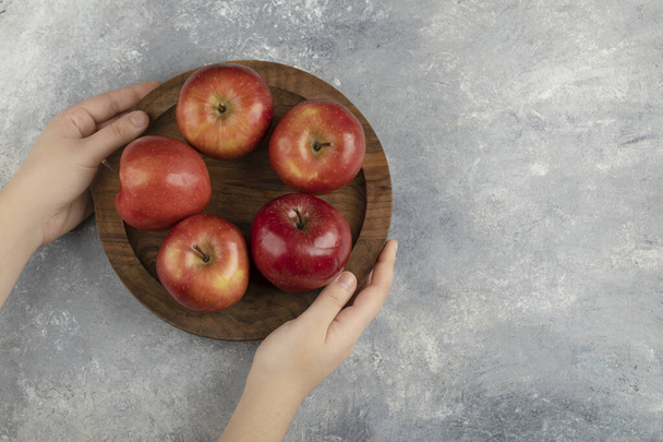 Vrouwelijke handen met houten plaat rode appels op marmeren oppervlak. Hoge kwaliteit foto - Foto, afbeelding