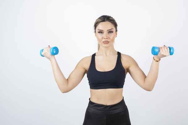 Blonde fit woman in black top standing and exercising with dumbbells . High quality photo - Fotografie, Obrázek