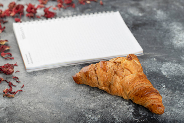 Tasty buttery croissant with opened notebook on stone table . High quality photo - Photo, Image