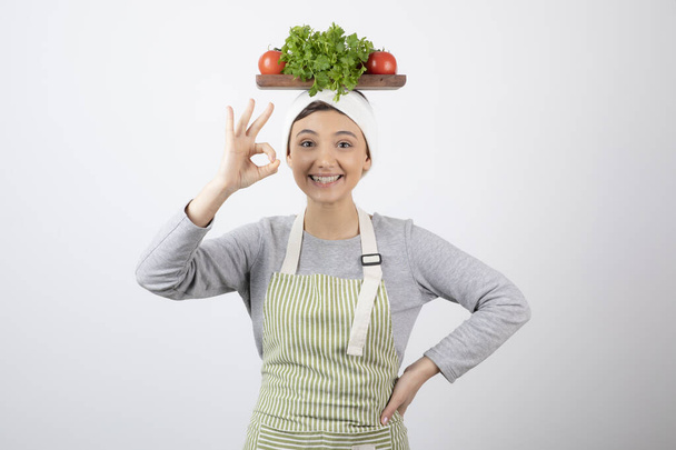 ［OK］をジェスチャーを示す頭の上に新鮮な野菜の木の板と女性モデル。高品質の写真 - 写真・画像