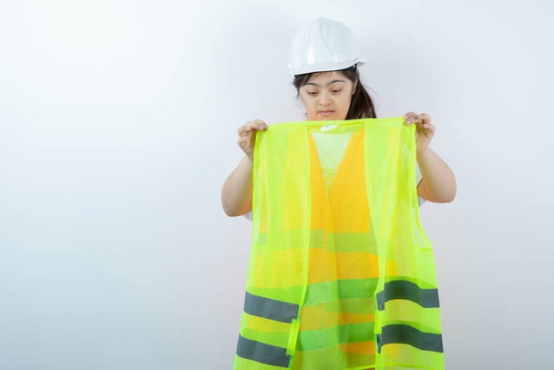 Joven trabajadora de la construcción en hardhat con chaleco sobre pared blanca. Foto de alta calidad - Foto, Imagen