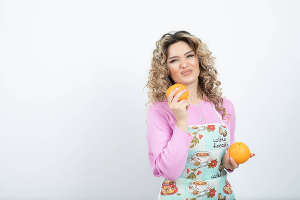 Portrait of young curly woman in apron posing with oranges. High quality photo - Фото, зображення