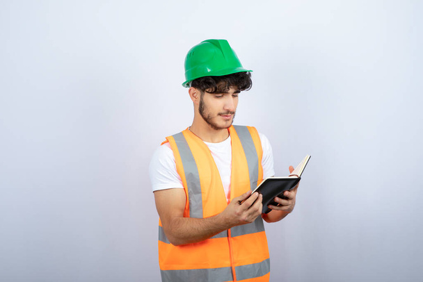 Mladý muž inženýr v zeleném klobouku čte poznámky na bílém pozadí. Kvalitní fotografie - Fotografie, Obrázek