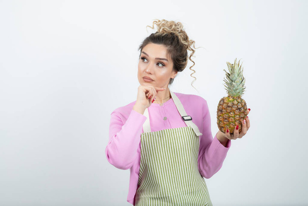 Jeune femme en tablier montrant de l'ananas frais mûr. Photo de haute qualité - Photo, image