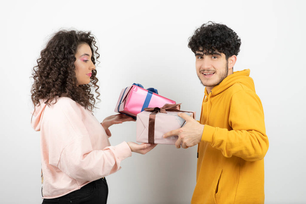 Portrait of young couple exchanging gifts for early holiday over white wall. High quality photo - Photo, Image