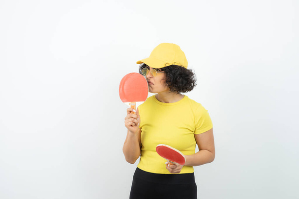 Portrait studio de jeune fille aux cheveux bouclés tenant des raquettes de ping-pong. Photo de haute qualité - Photo, image