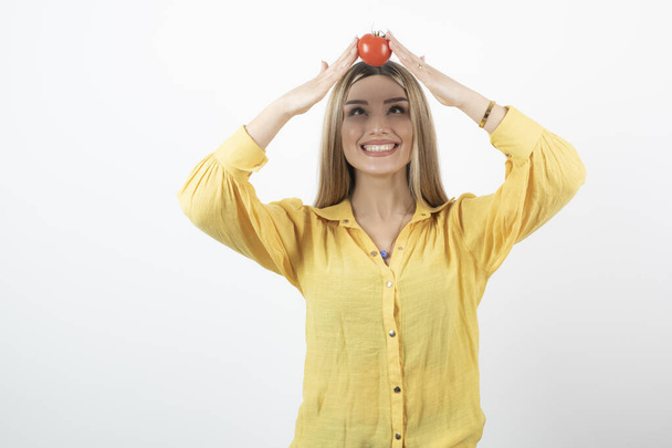 Usmívající se žena drží červené rajče na hlavě přes bílou zeď. Kvalitní fotografie - Fotografie, Obrázek